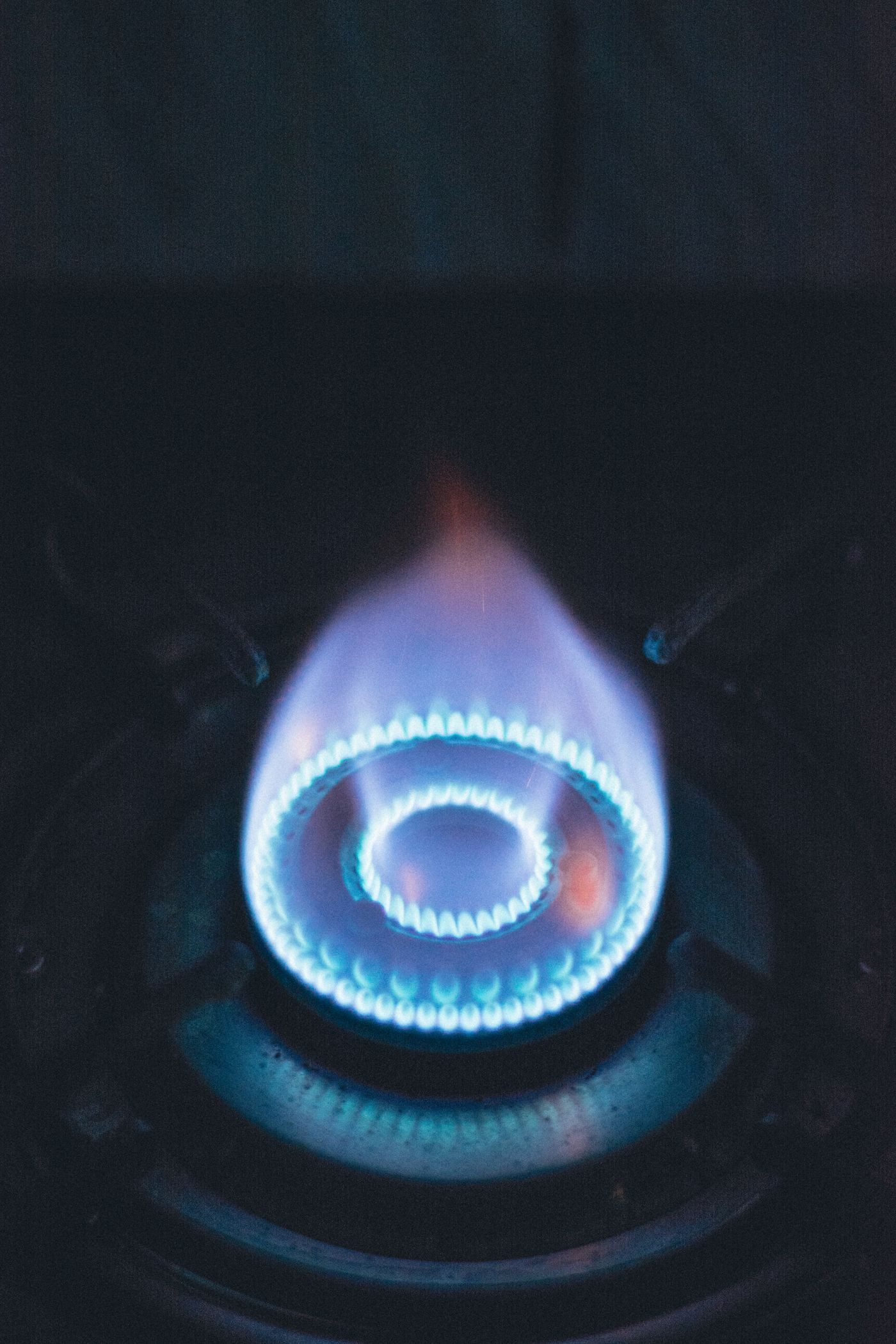 Close-up of a blue gas burner flame on a hob against a dark background