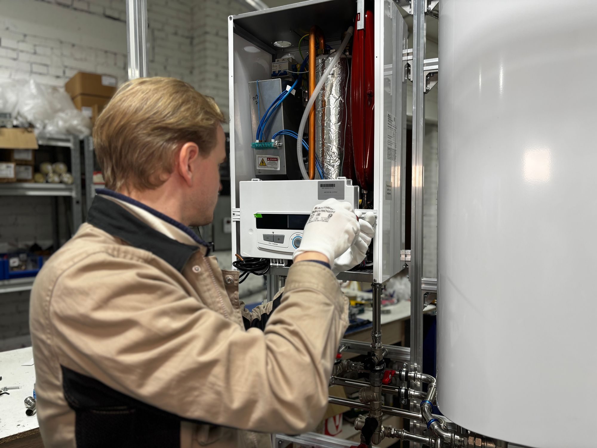 Gas engineer in work gloves adjusting the controls of a wall-hung combi boiler with the casing off