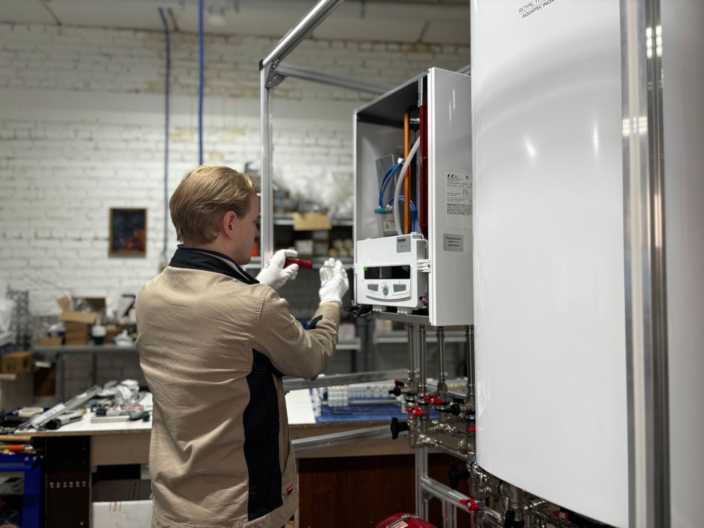 Engineer working on an open combi boiler beside a hot water cylinder