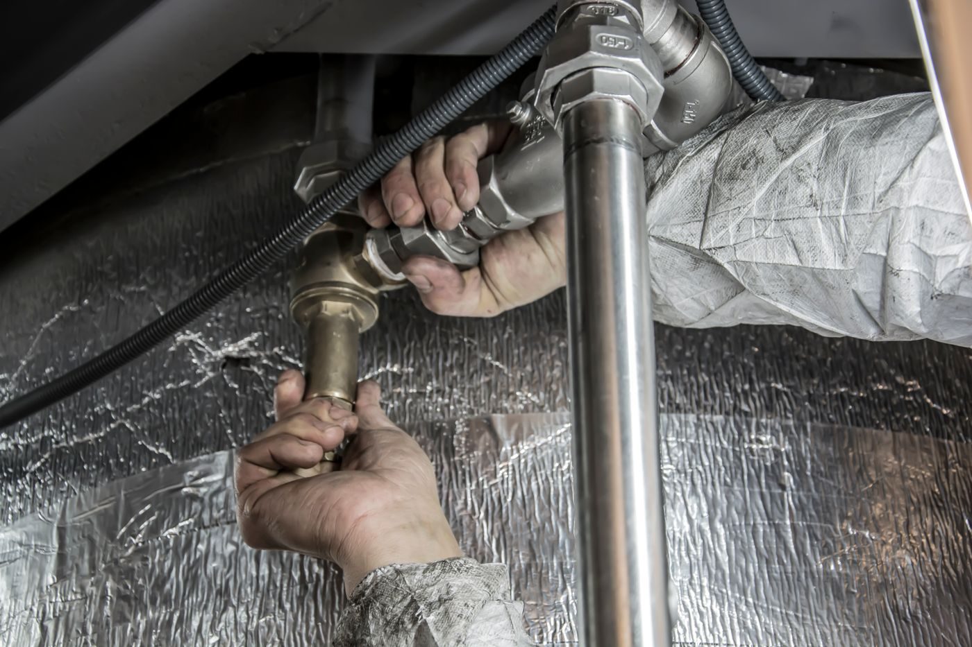 Hands tightening a steel pipe joint with a wrench beside insulated ducting